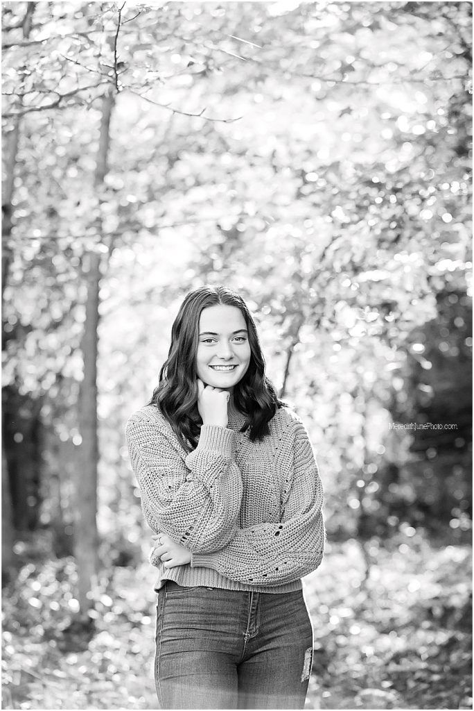 Person in a cozy knit sweater and jeans poses outdoors in a wooded setting with soft autumn lighting.
