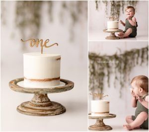 Simple white cake with gold 'one' topper on rustic wooden cake stand for first birthday celebration.