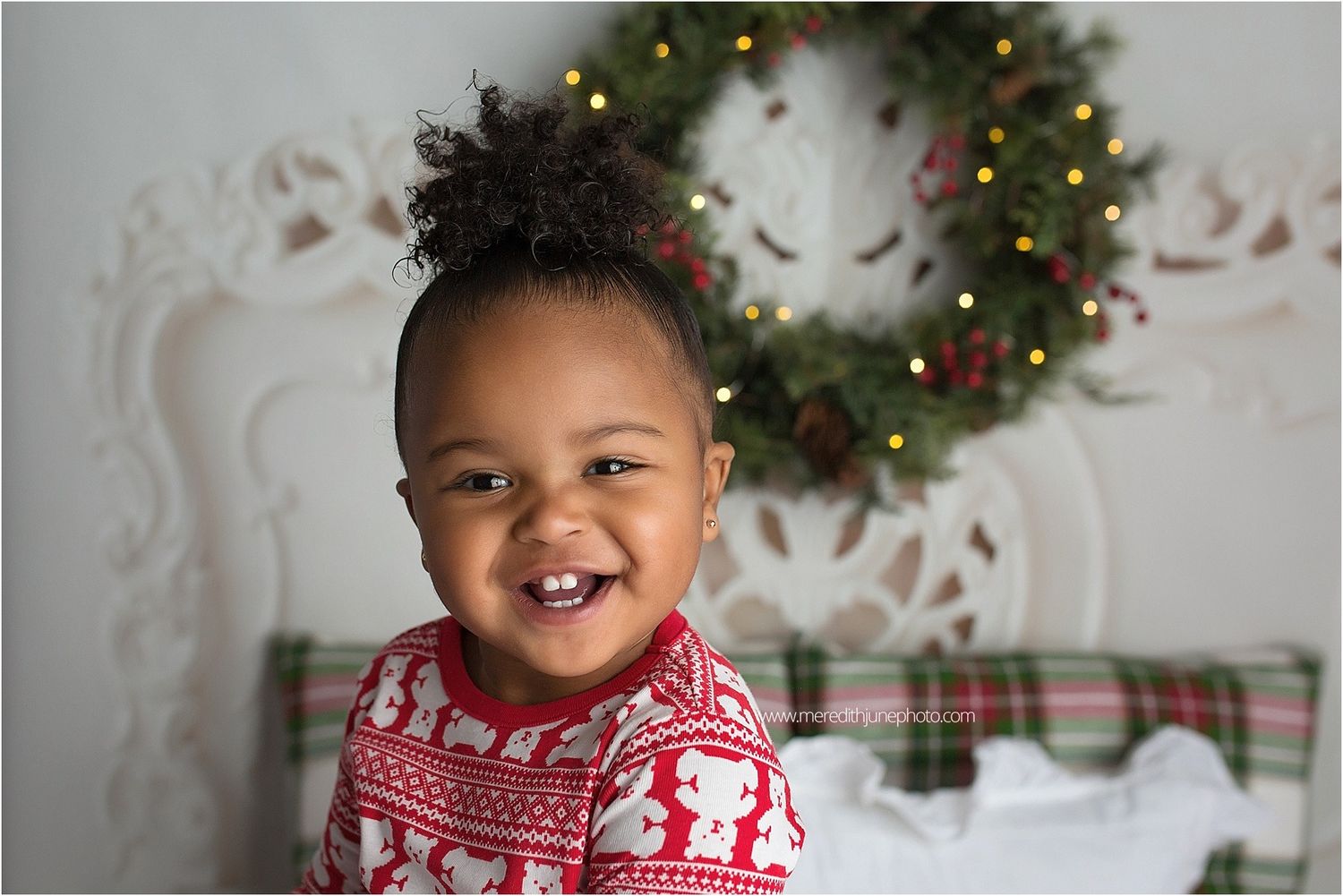 Child wearing festive red and white patterned scarf smiles near Christmas decorations.