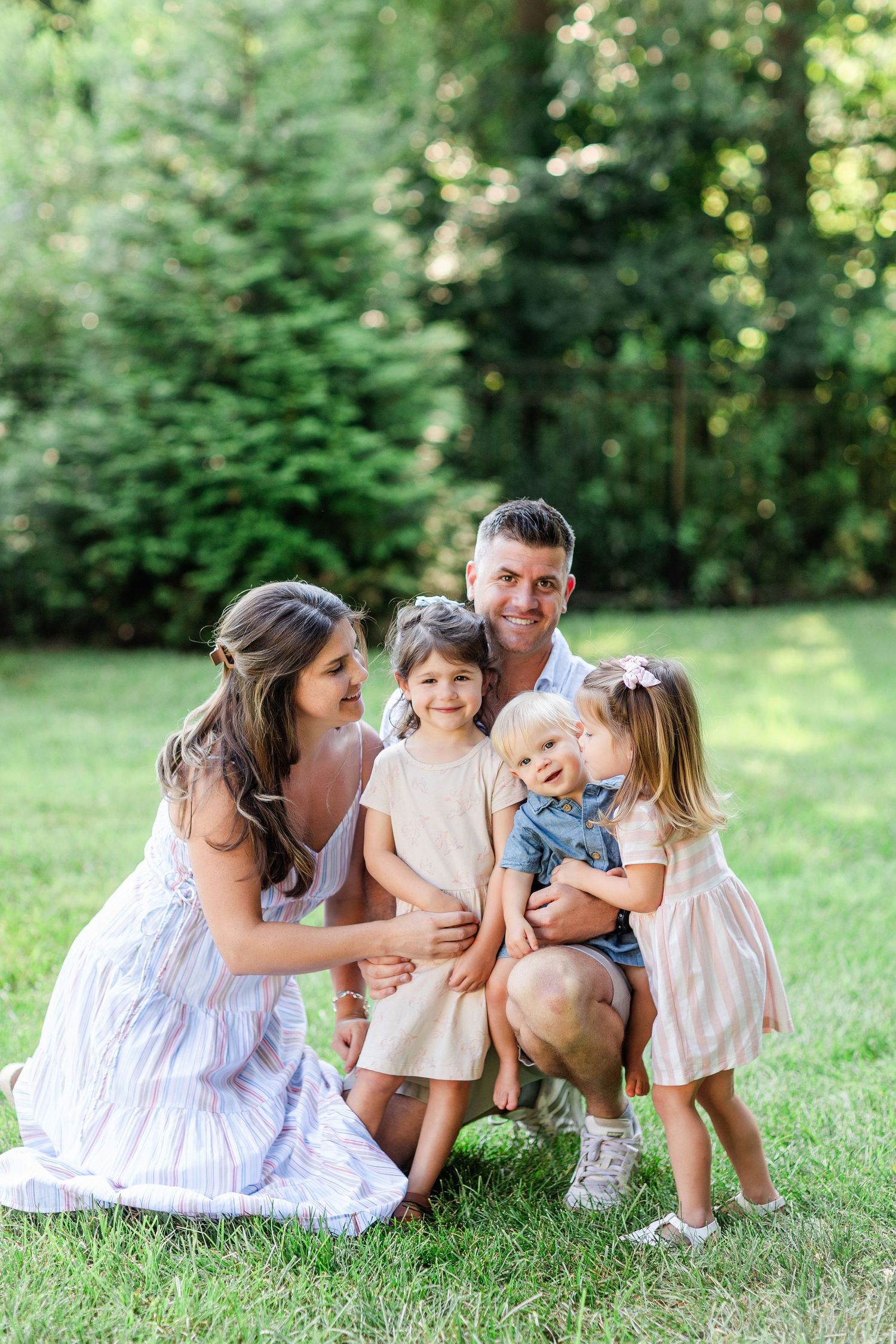Family laughing and playing together on grass during summer photo session.