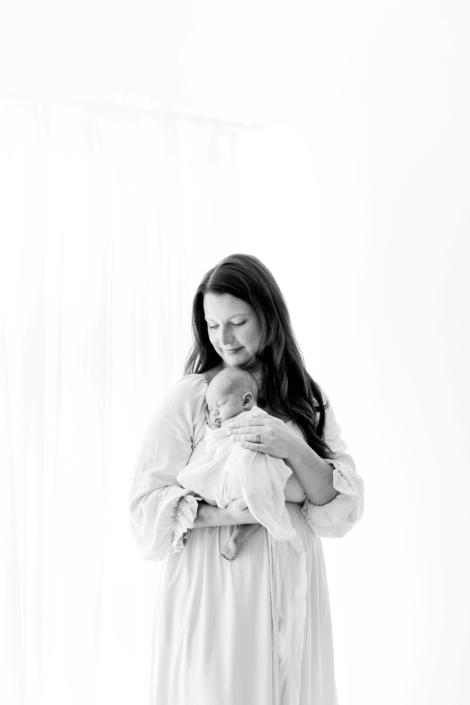 A series of tender black and white photos showing a parent embracing a baby in white clothing.