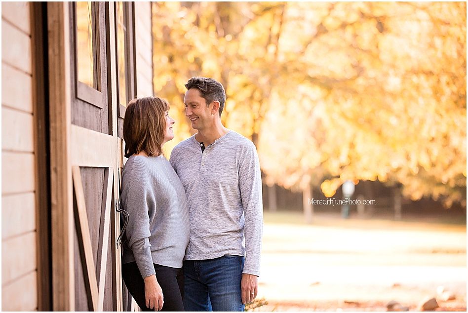 A couple stands in a doorway with autumn foliage creating a warm golden backdrop in the background.