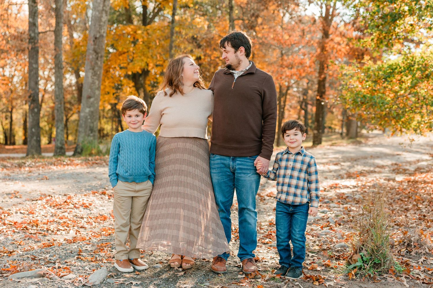 Family walking together through autumn forest with orange and yellow fall foliage on ground.