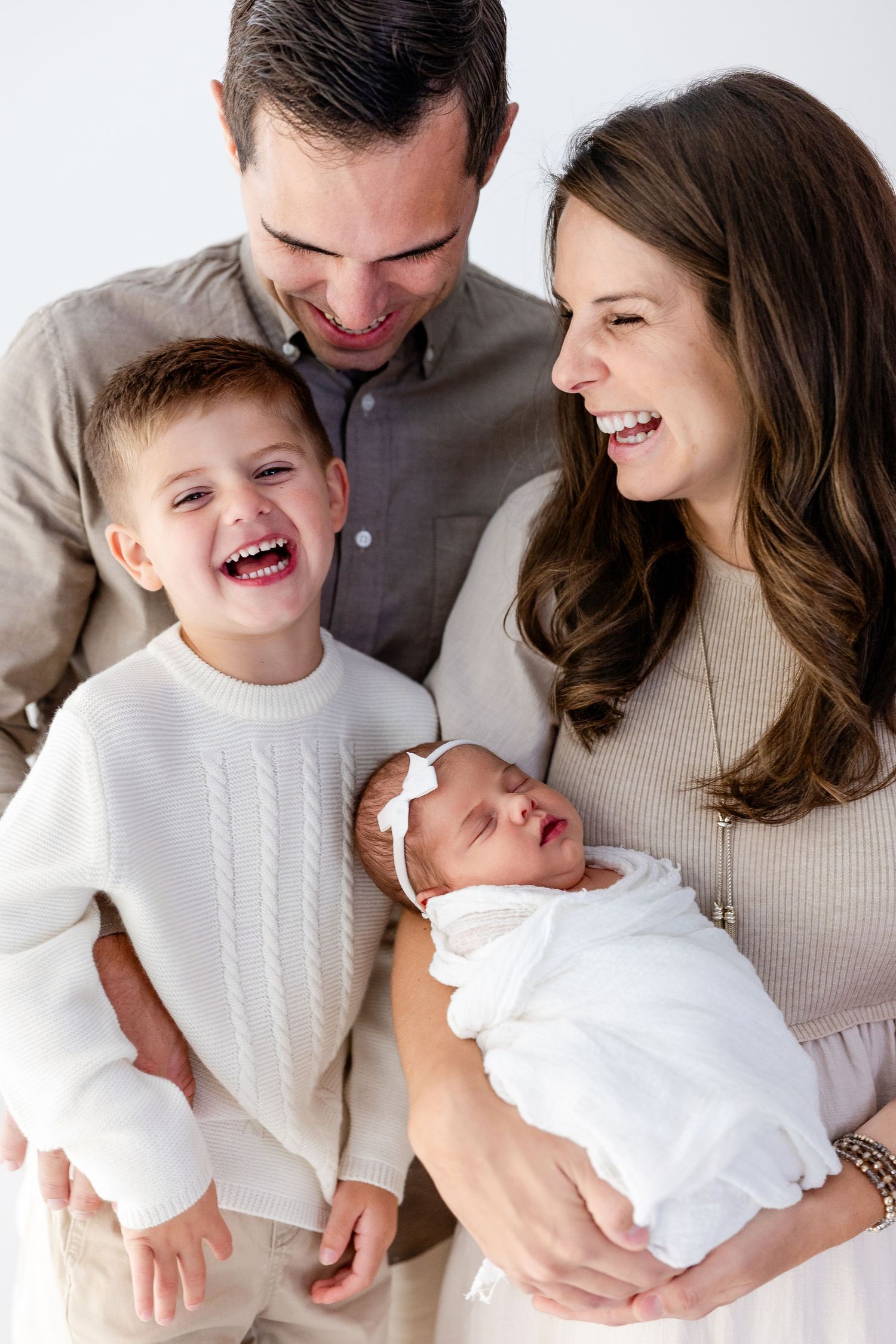 Family shares joyful moments together in coordinated neutral outfits against white backdrop.