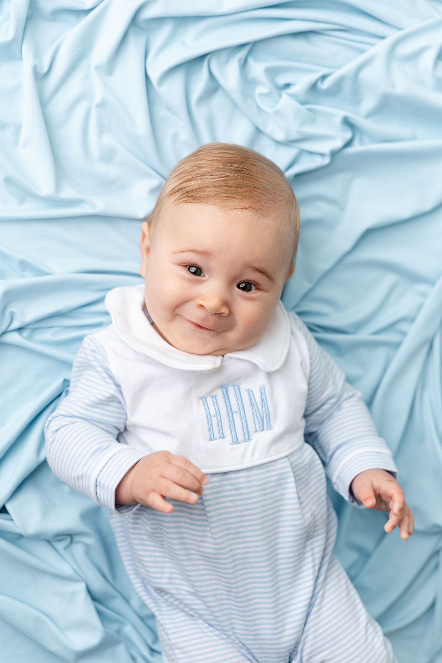 Baby wearing blue and white striped outfit lying on light blue blanket in progression of sweet expressions.