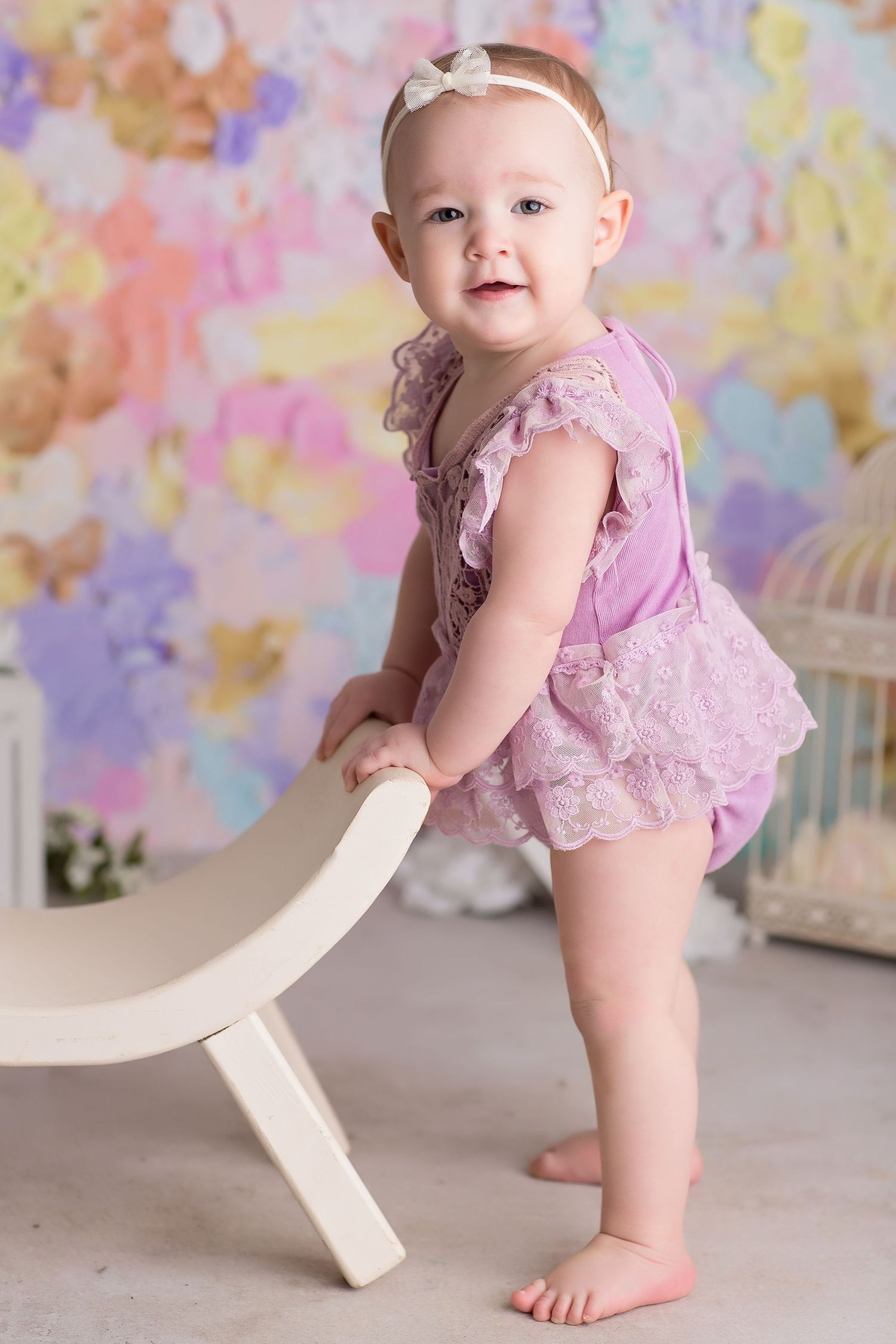 Baby in pink lace dress poses against colorful pastel butterfly backdrop.