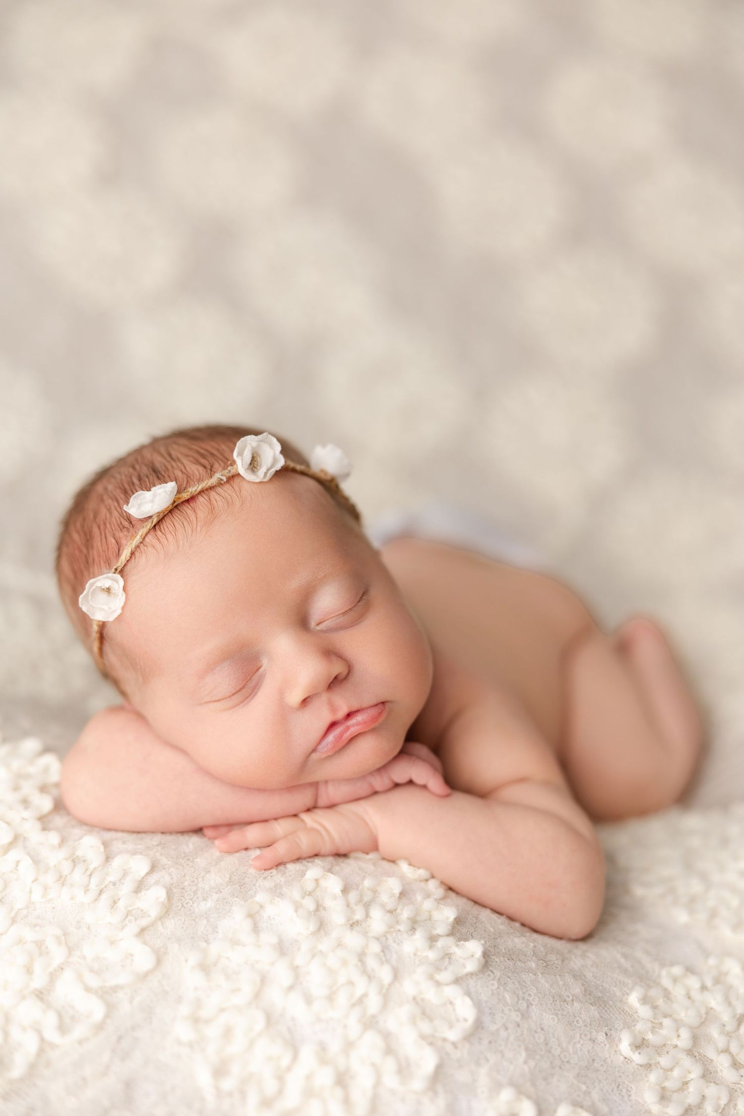 Peaceful newborn baby sleeping on soft white textured blanket wearing delicate floral headband.