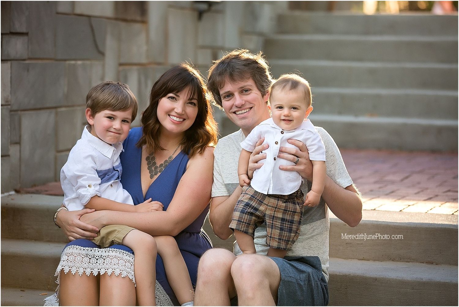 A family sits together on outdoor stone steps during golden hour lighting.