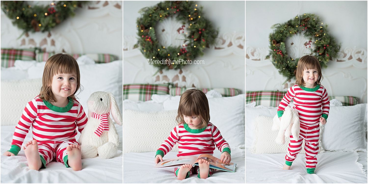 Child in red and white striped holiday pajamas sits on white bedding playing with Christmas decorations.