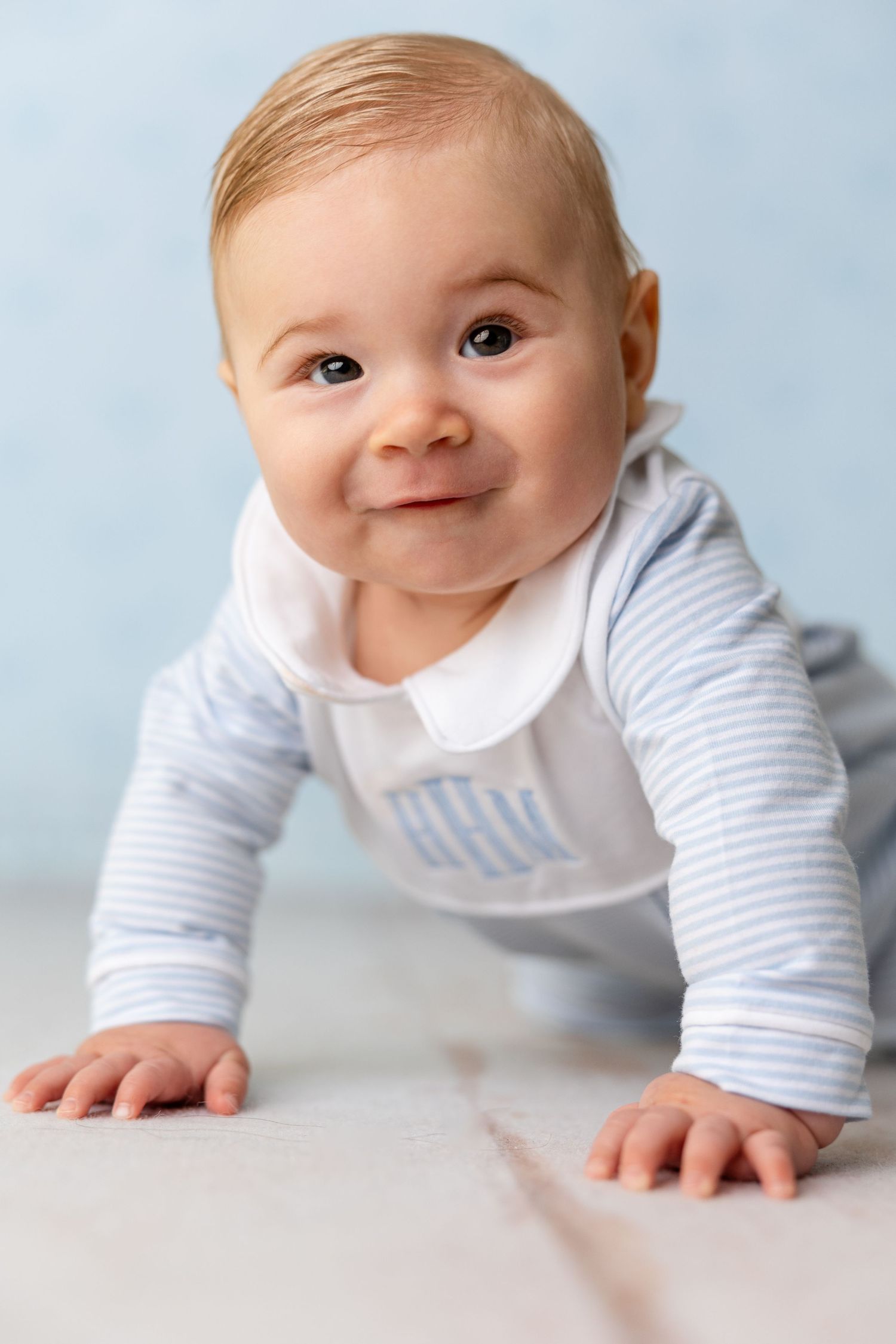 Baby in white and blue striped outfit practices crawling on light surface.