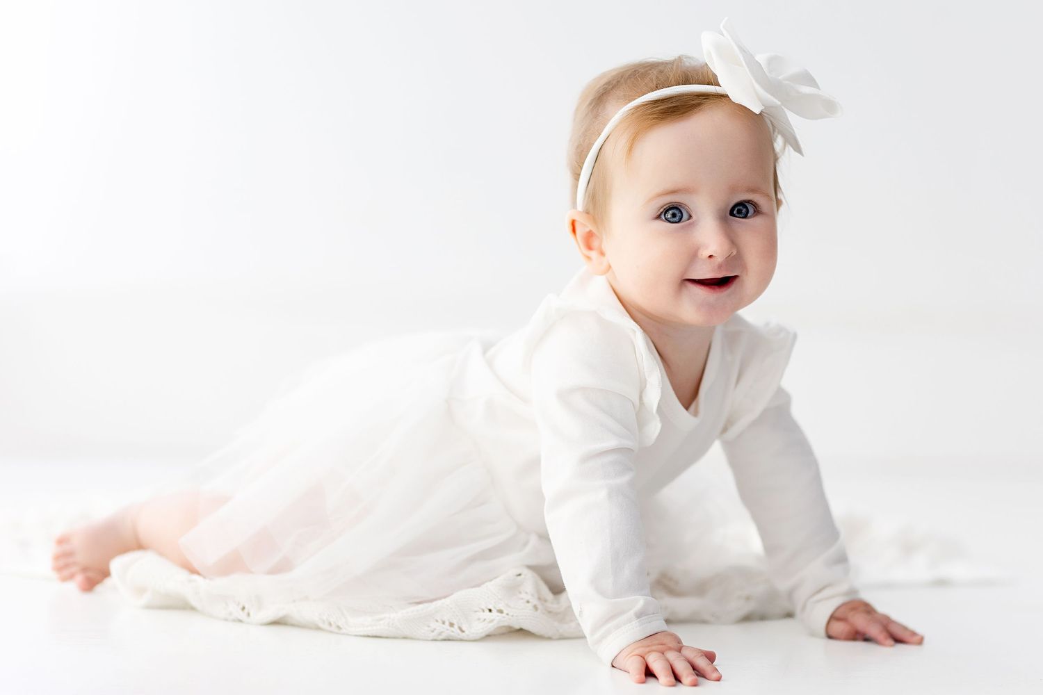 Baby in white outfit crawling and playing on light background in progression of shots.