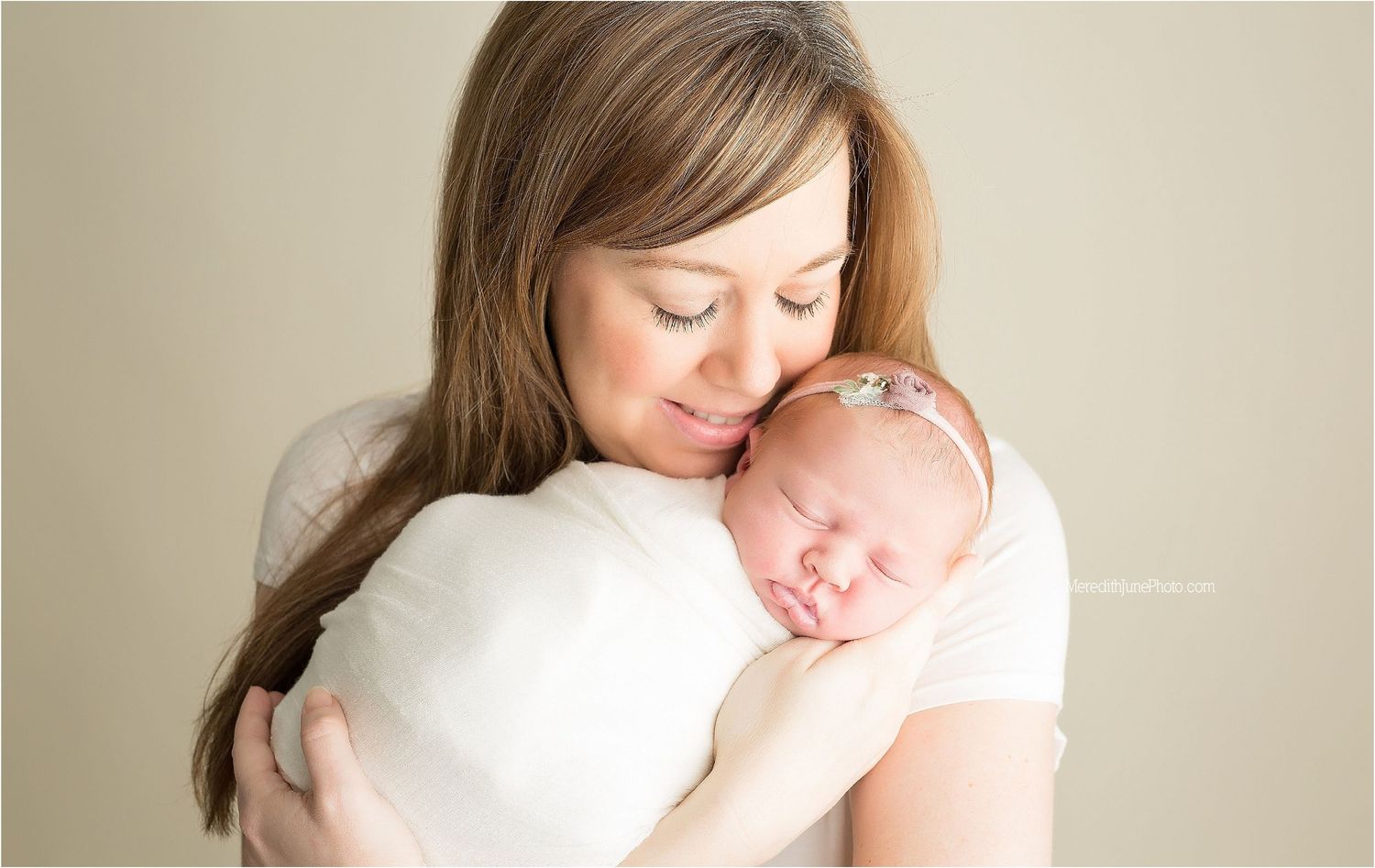 A tender moment between parent and sleeping newborn in soft natural light against neutral background.