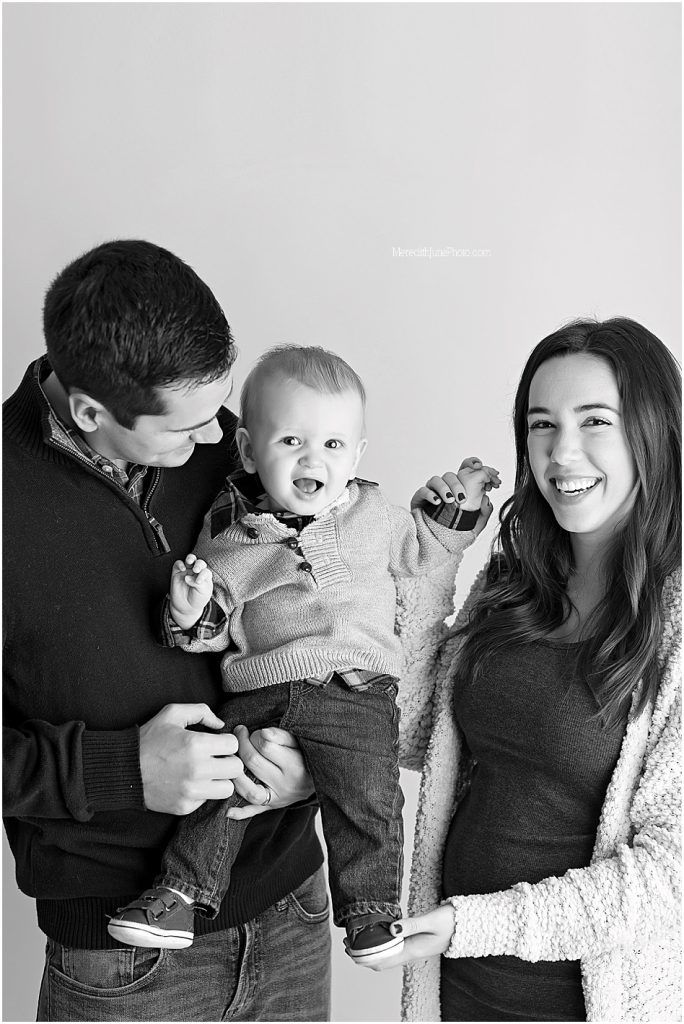A joyful black and white family portrait showing parents with their smiling baby in casual winter attire.