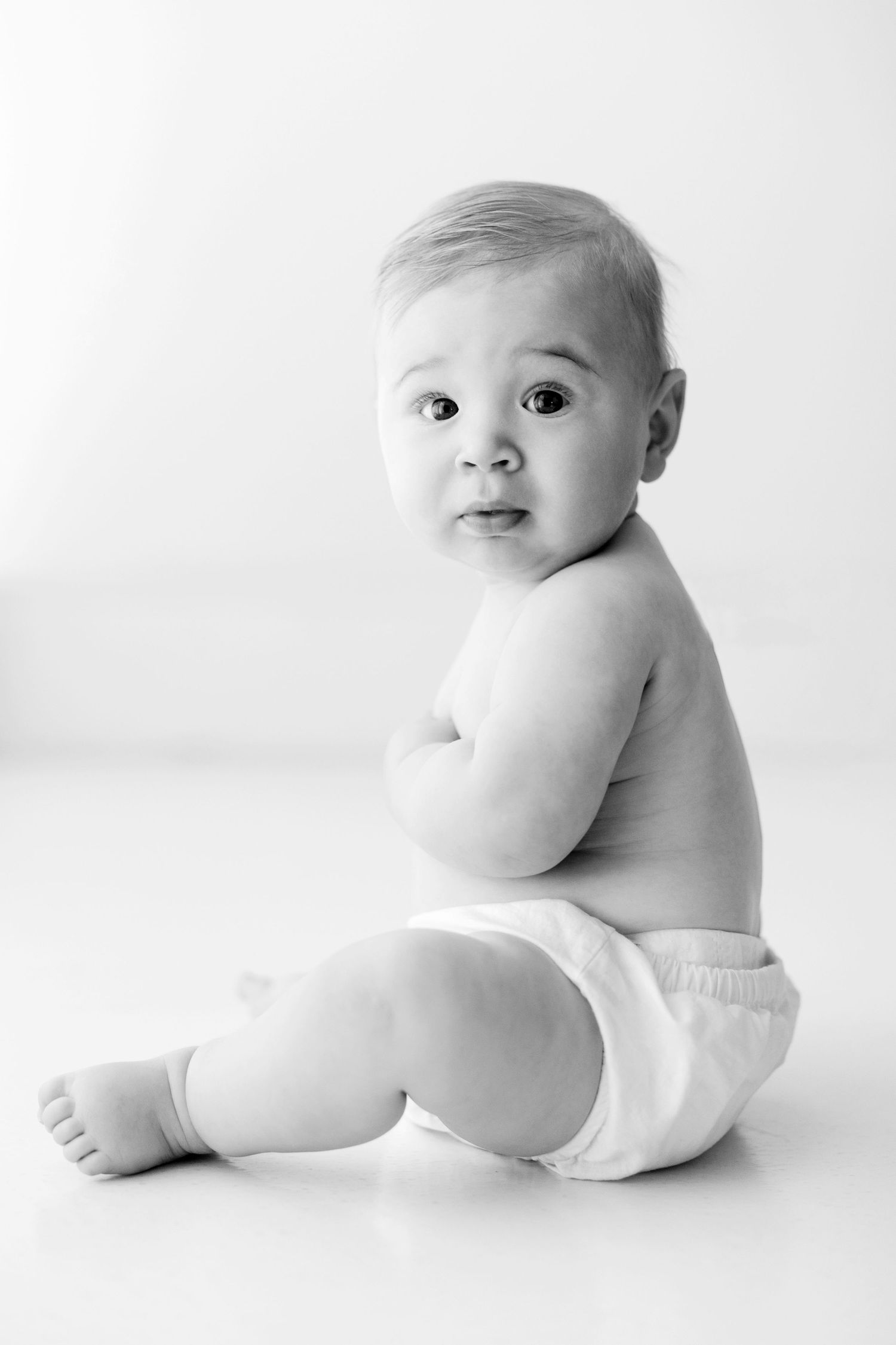 Artistic black and white photos of an infant in a diaper against white background in various positions.