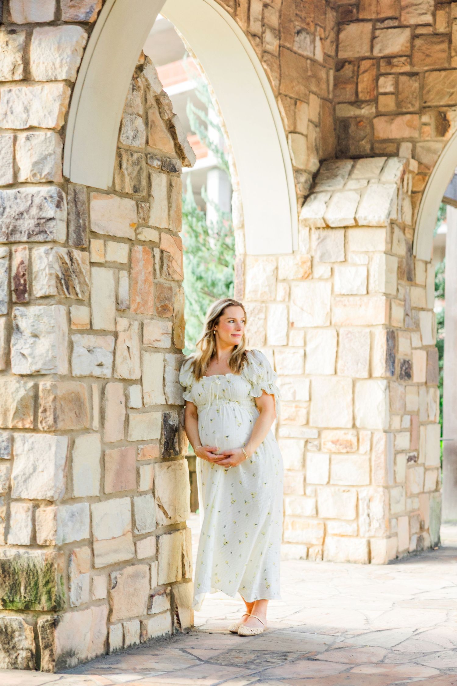 A figure in a white dress poses in a stone archway corridor with natural lighting filtering through the arches.