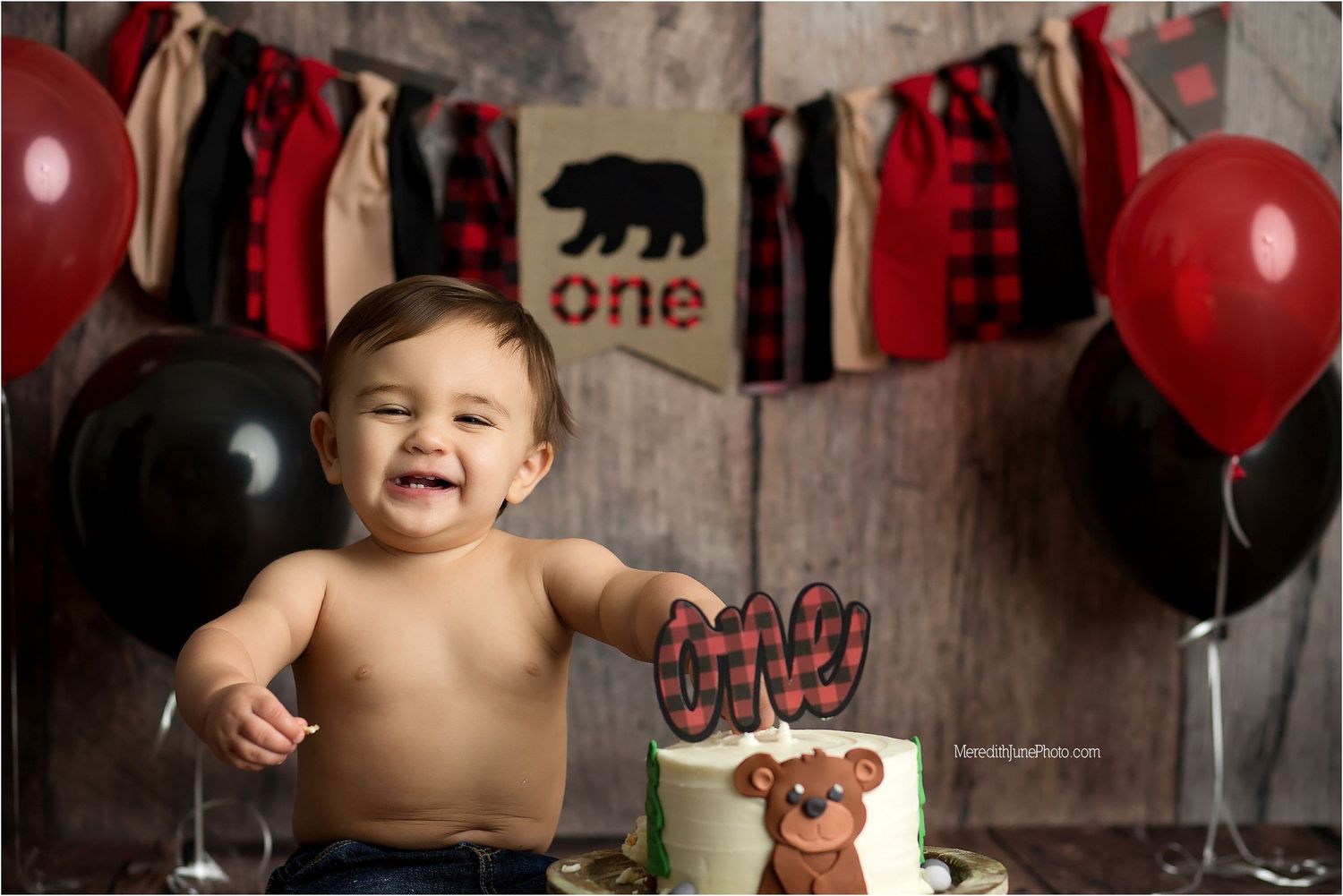 A baby's first birthday cake smash photo session with red balloons and rustic wooden backdrop.
