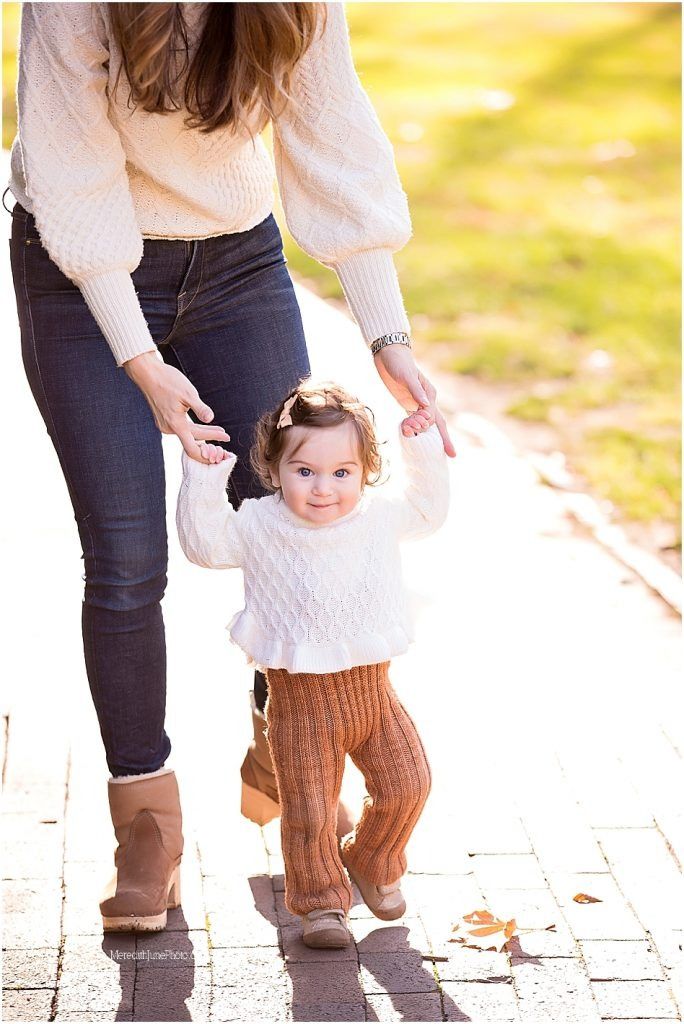 Parent and toddler walking together on brick path during golden hour autumn photoshoot.