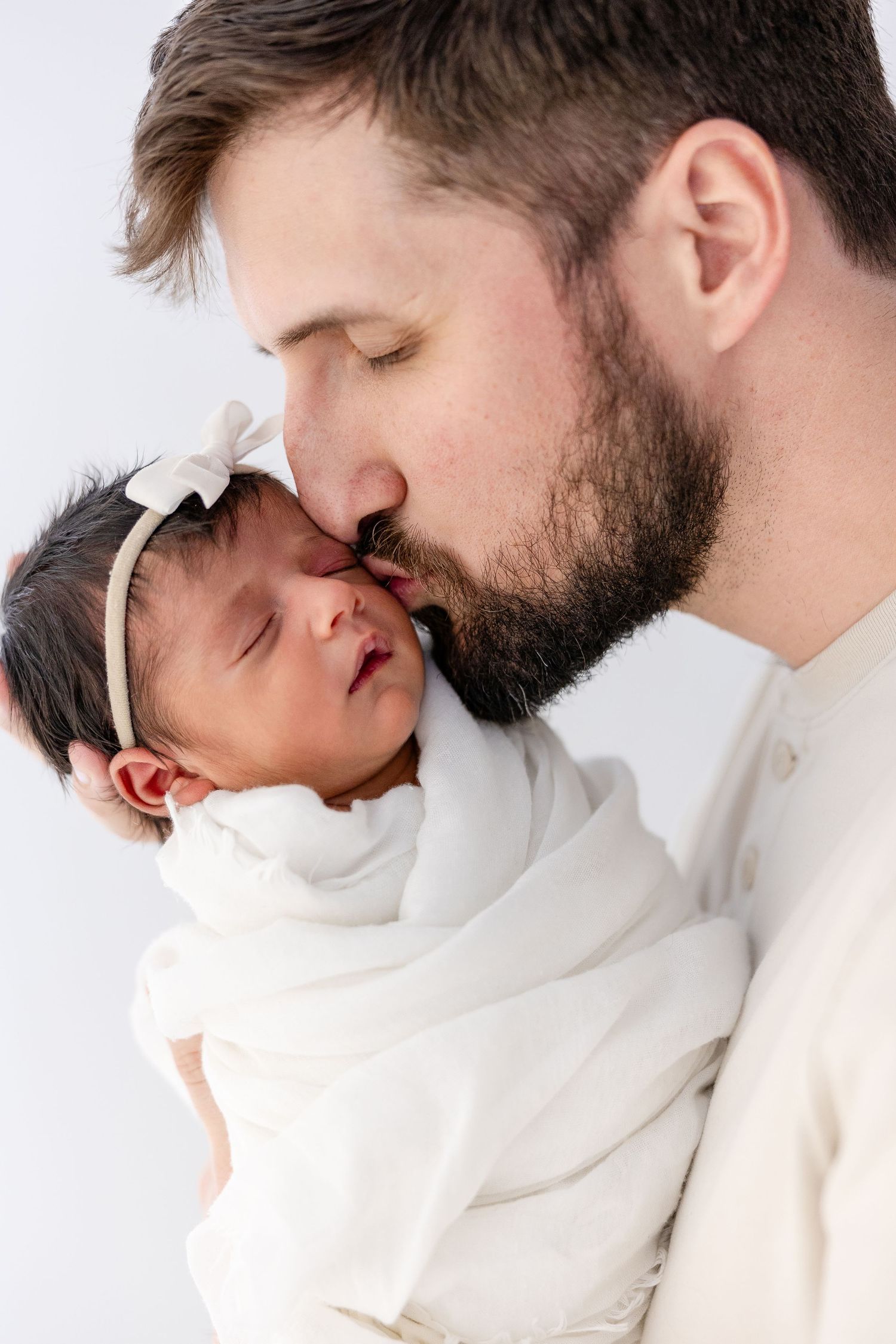 Intimate close-up portraits of parent and baby in white clothing against a light background.
