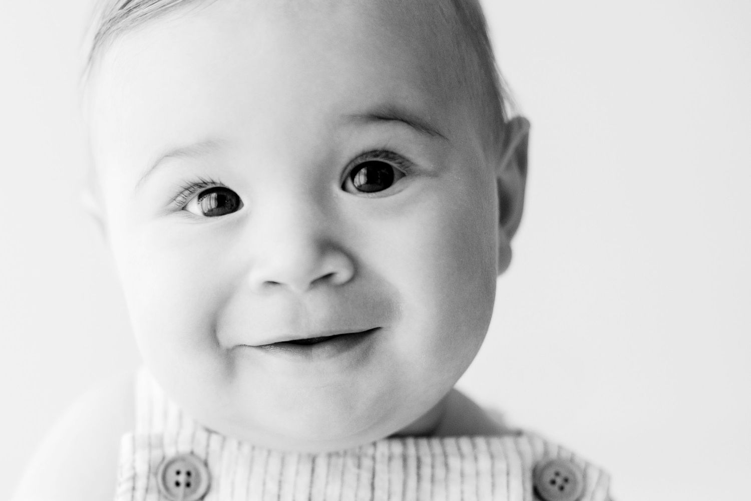 Black and white close up portrait of a smiling baby wearing a knit sweater.