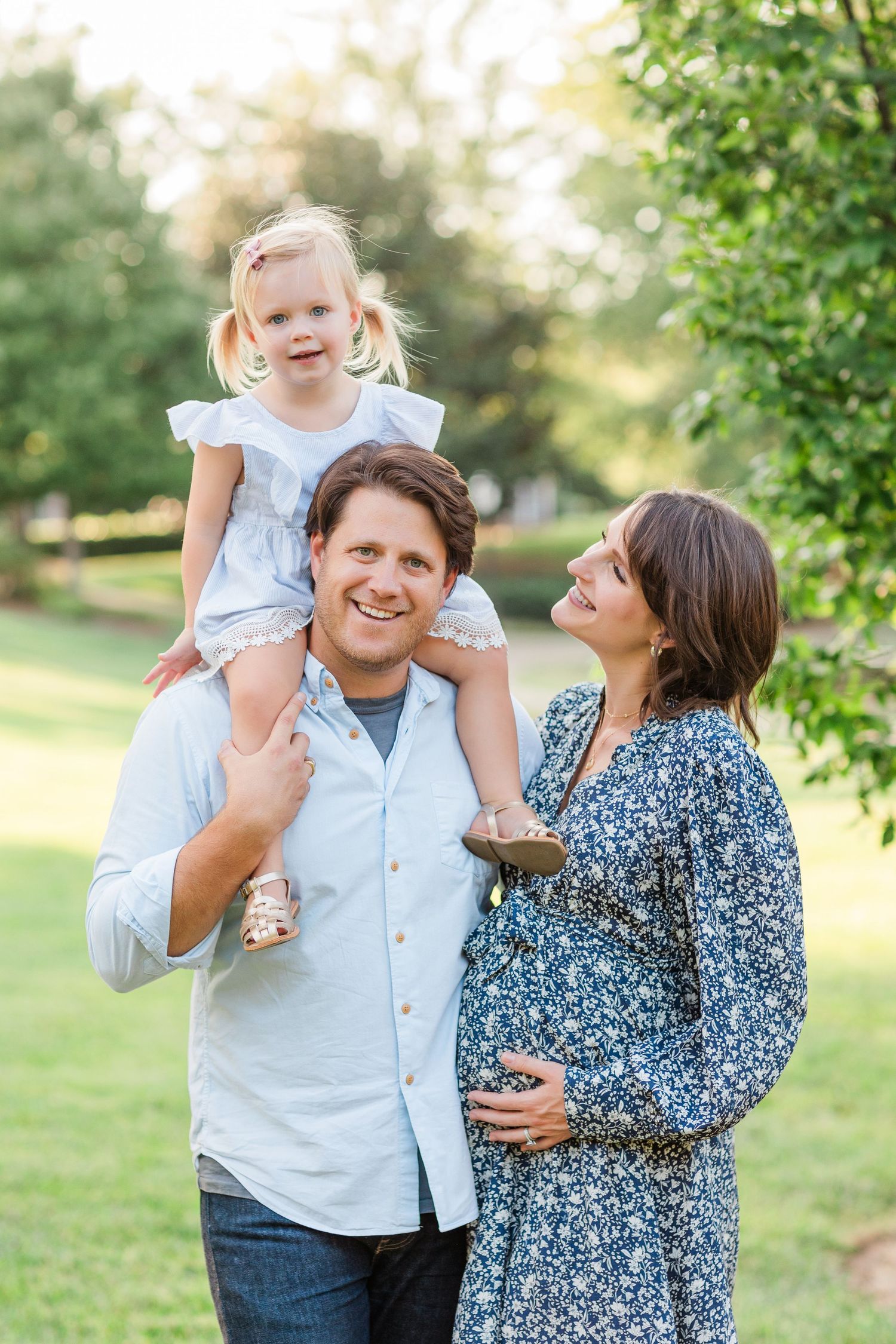 Family portrait series in a sunny park with parents and child sharing playful moments together.