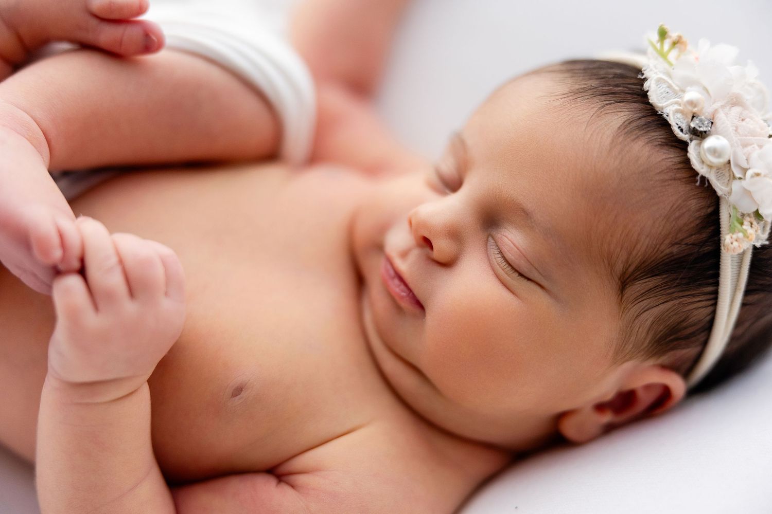 Sleeping newborn wearing delicate lace headband in soft natural light.