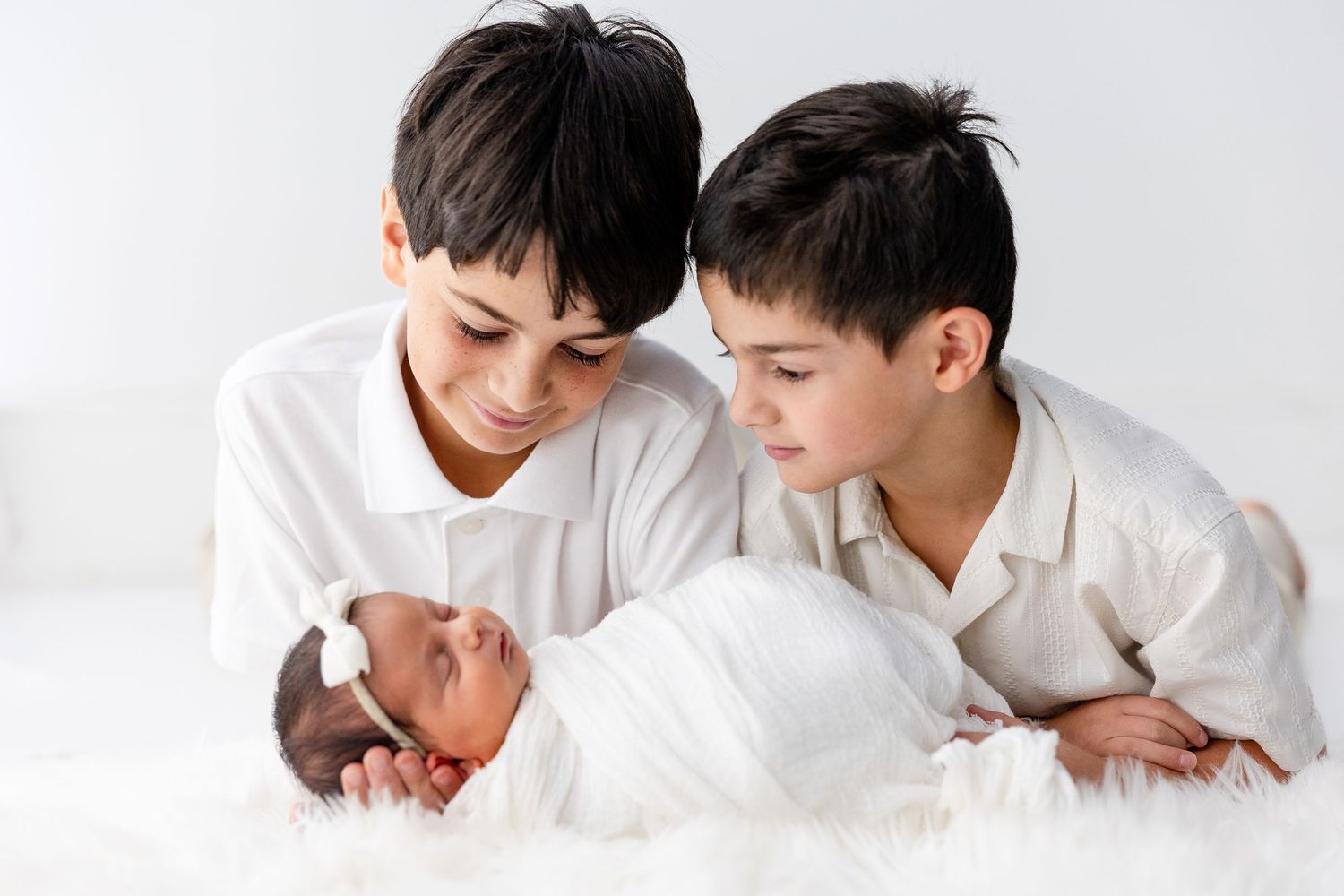 Black and white family photo series showing siblings bonding with new baby.