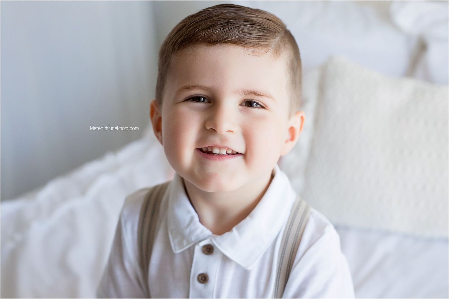 Child wearing white polo shirt smiles while sitting against light background.