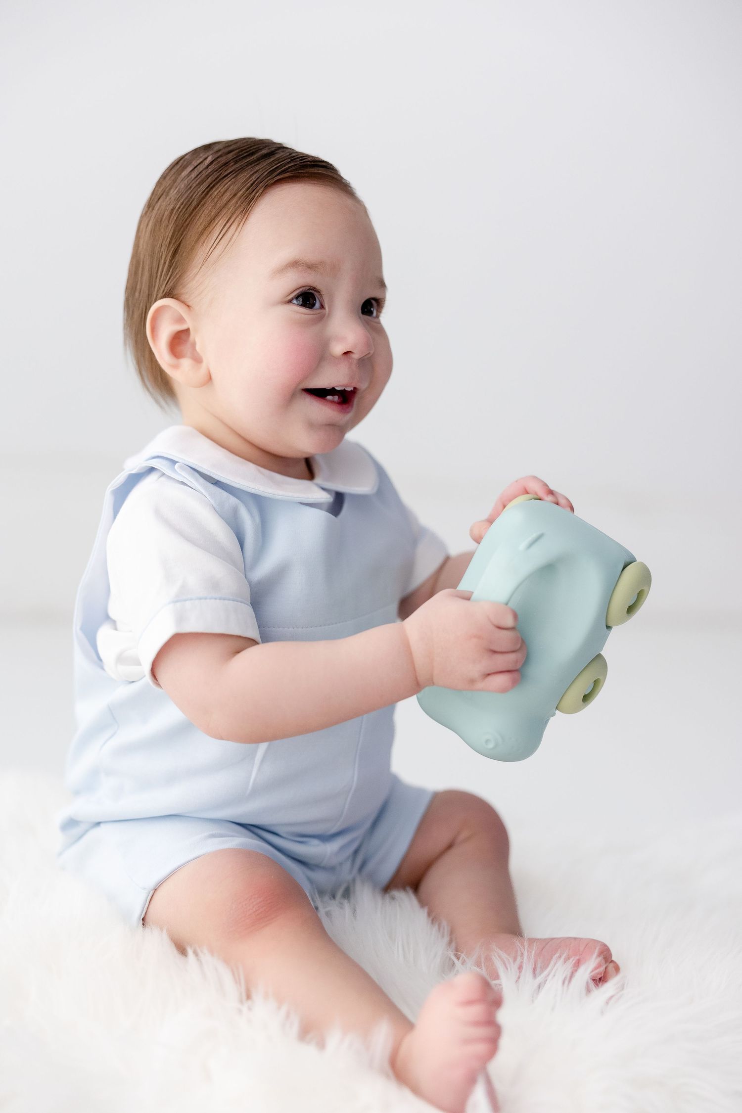 Baby in white onesie plays with light blue teacup while sitting on white background.
