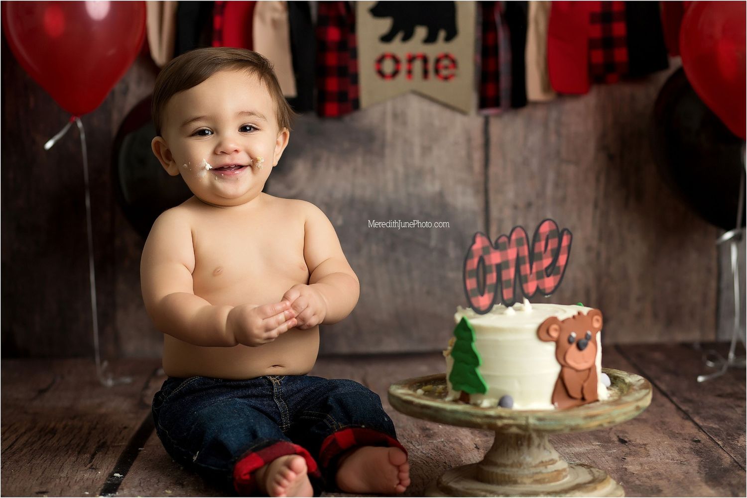 A first birthday celebration setup with a rustic woodland theme featuring a small cake and red balloon decorations.