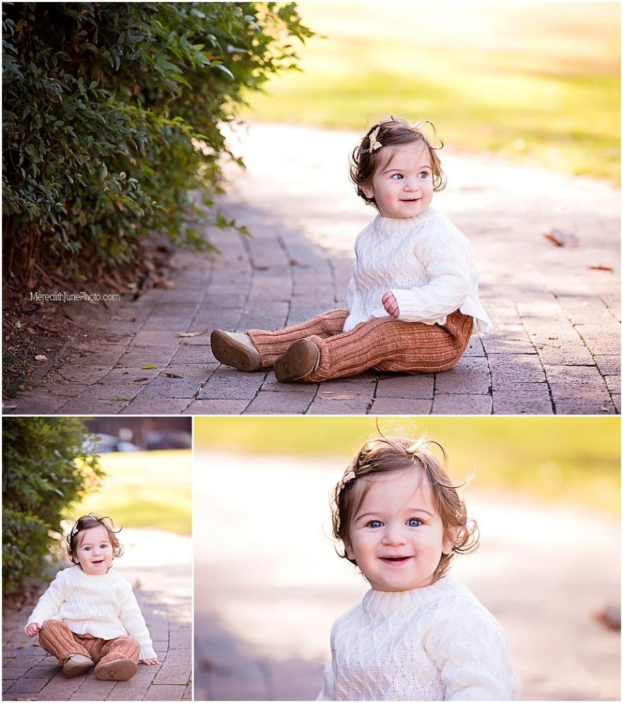Sweet toddler in white sweater and brown pants sitting on brick path during outdoor photoshoot.