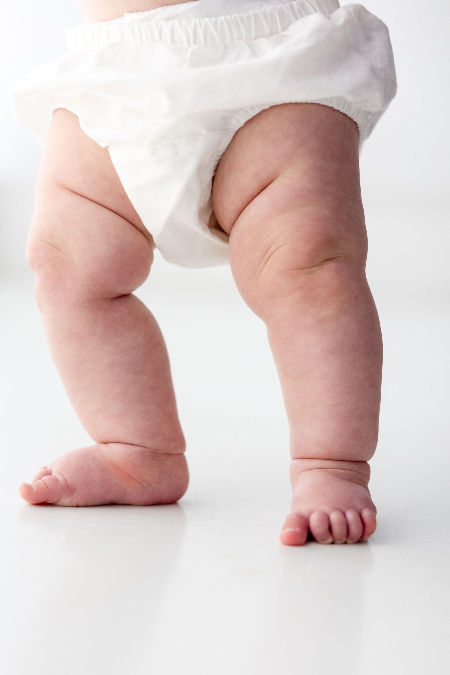 Close-up series of chubby baby legs and feet in white diaper walking on white surface.