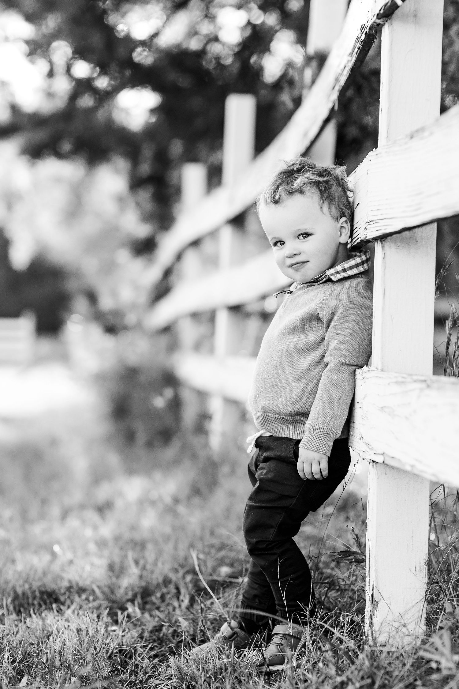 Black and white photos of toddler exploring white picket fence outdoors.
