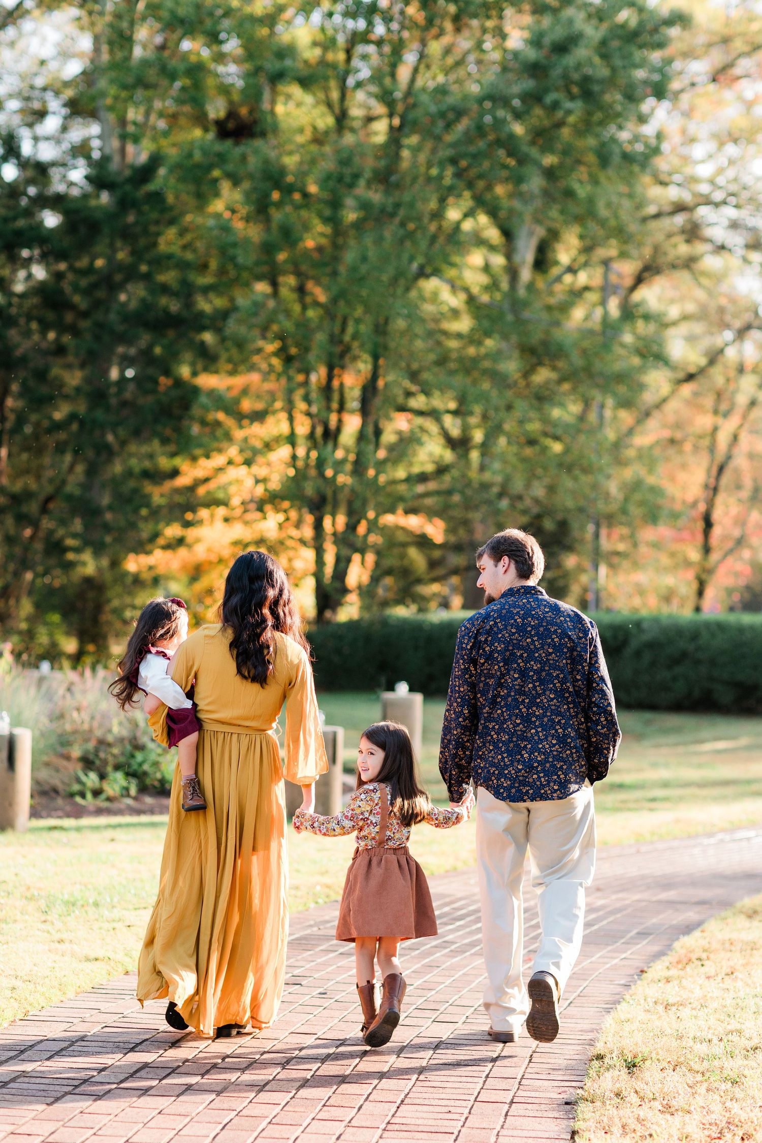 Family walking together on a brick path surrounded by autumn trees in golden sunlight.