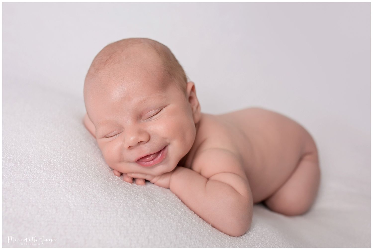 A sleeping newborn baby curled up peacefully on soft white blankets in a professional studio setting.