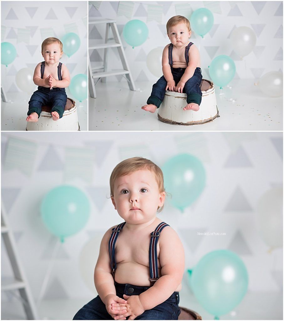 Baby in navy blue outfit sits among mint green balloons during first birthday photo session.