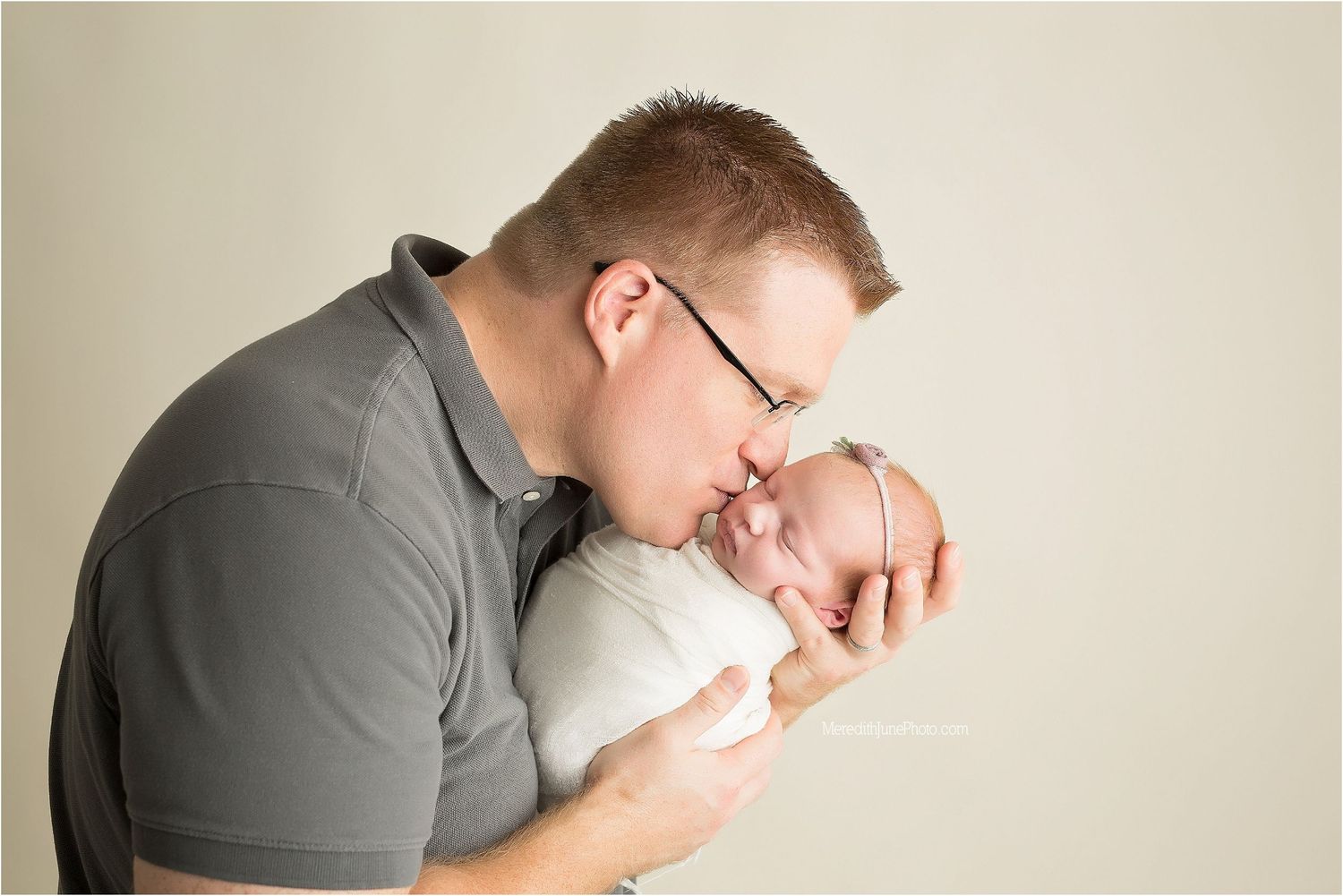 A tender newborn photography session shows a gentle embrace against a light neutral background.