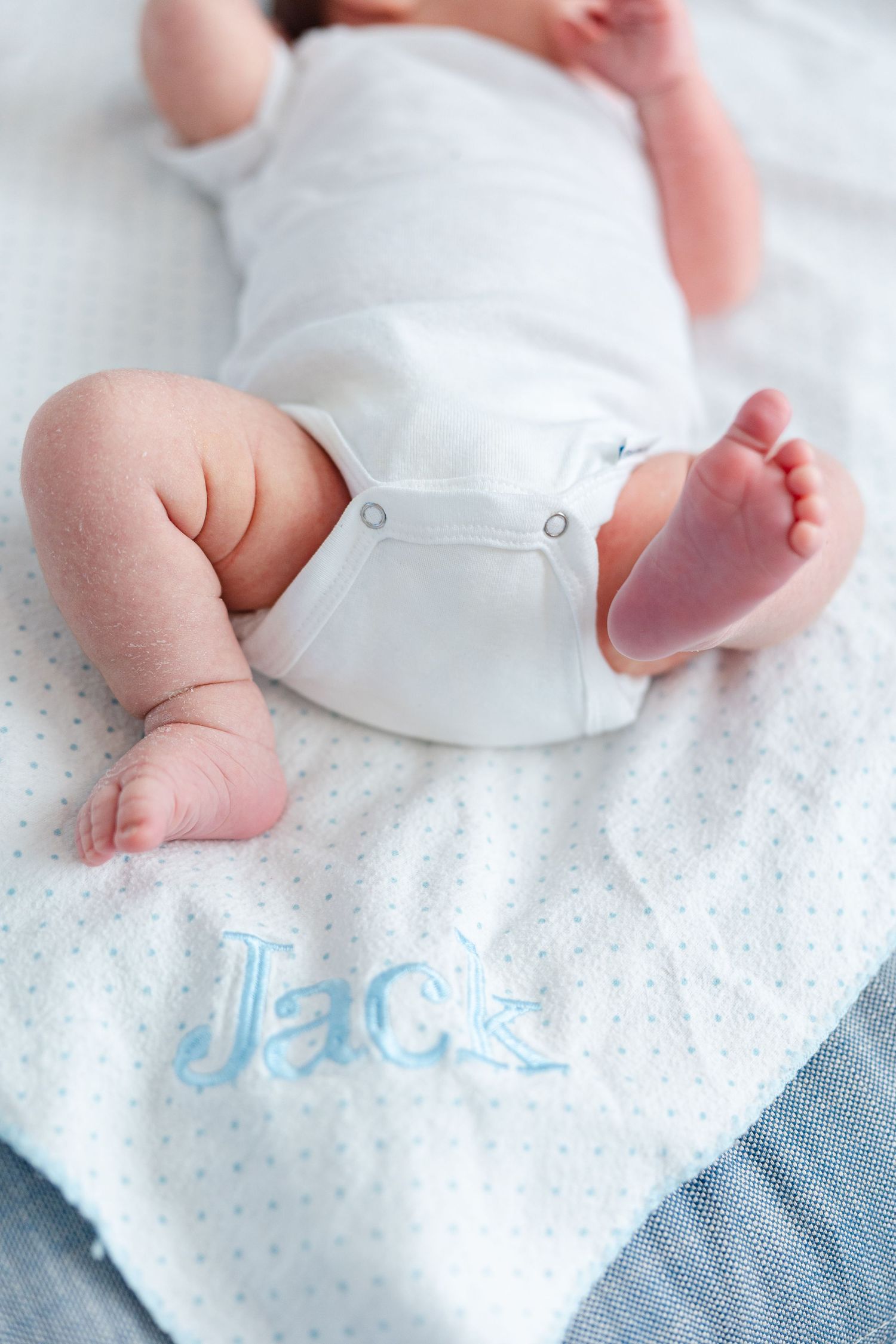 Close-up details of a baby wearing white clothing on polka dot fabric showing tiny hands and feet.