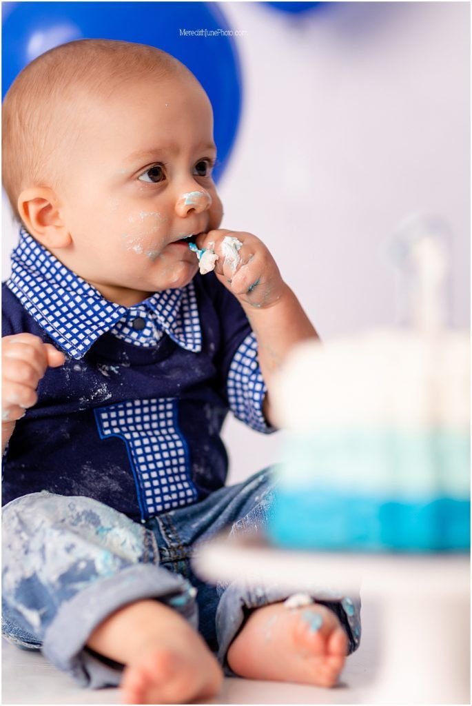 Baby wearing a blue polka dot bowtie and denim outfit sitting against a light background.