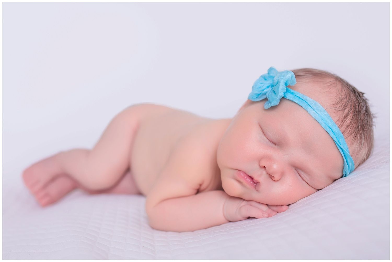 Peaceful sleeping newborn baby wearing light blue headband lying on soft white blanket.