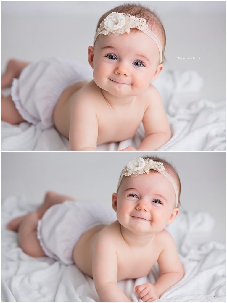 Sweet baby in white lace headband lying on soft white blanket smiling at camera in professional portrait session.