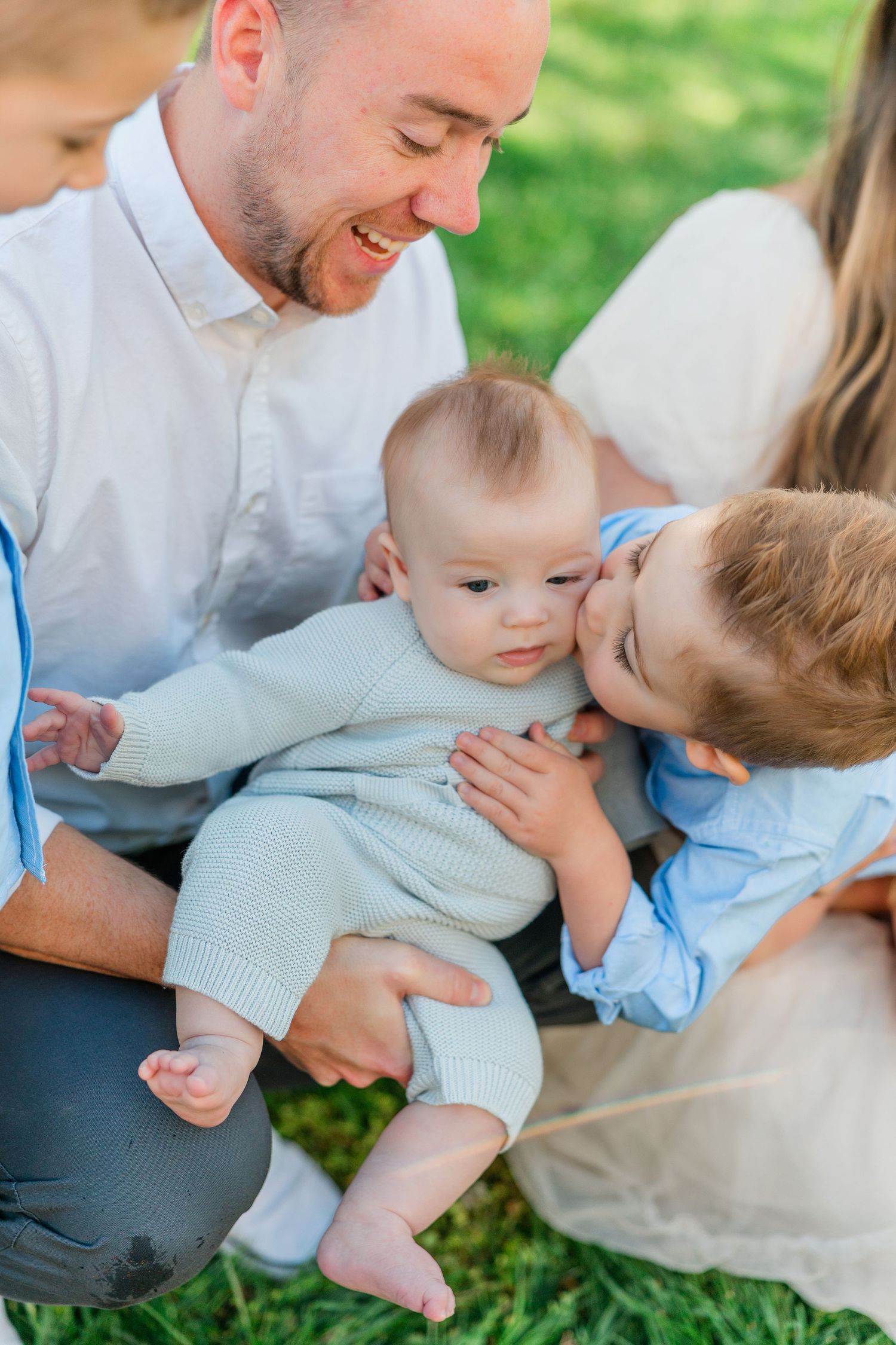 Sweet family portrait session outdoors showing tender moments between parents and children on grass.