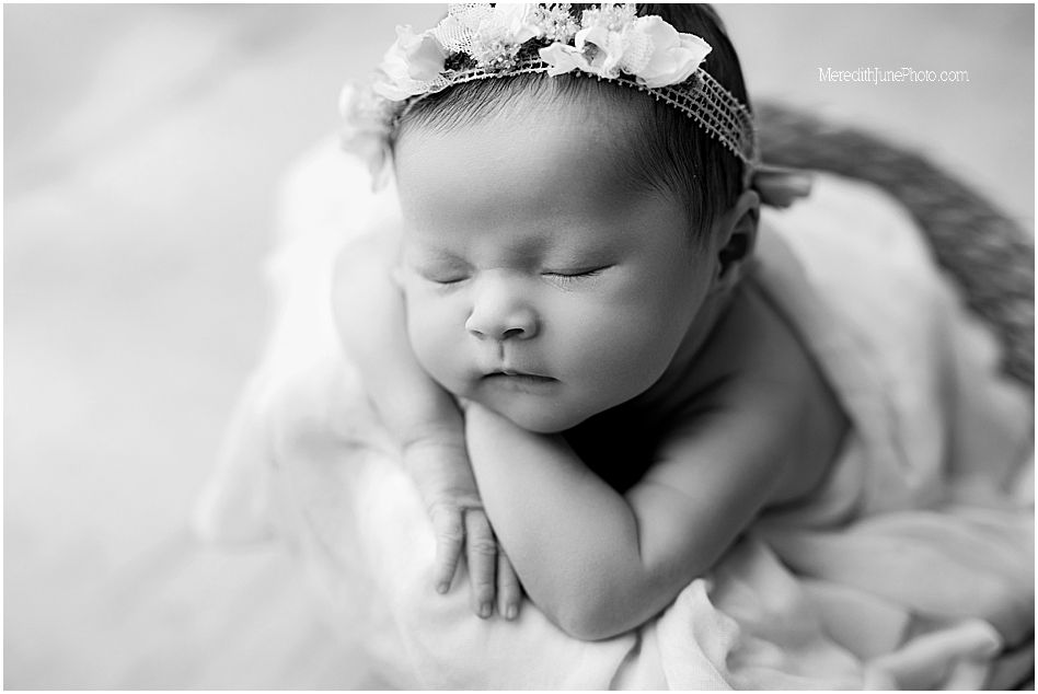 A sleeping newborn baby swaddled in white fabric rests peacefully in a monochromatic portrait.