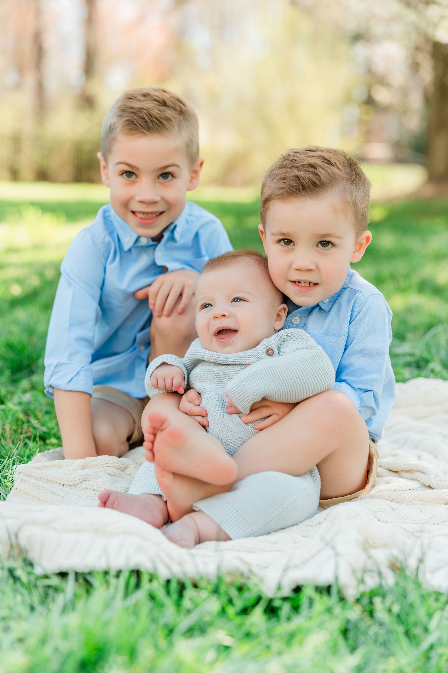 Three siblings sit together on a blanket in the grass during a spring photoshoot.