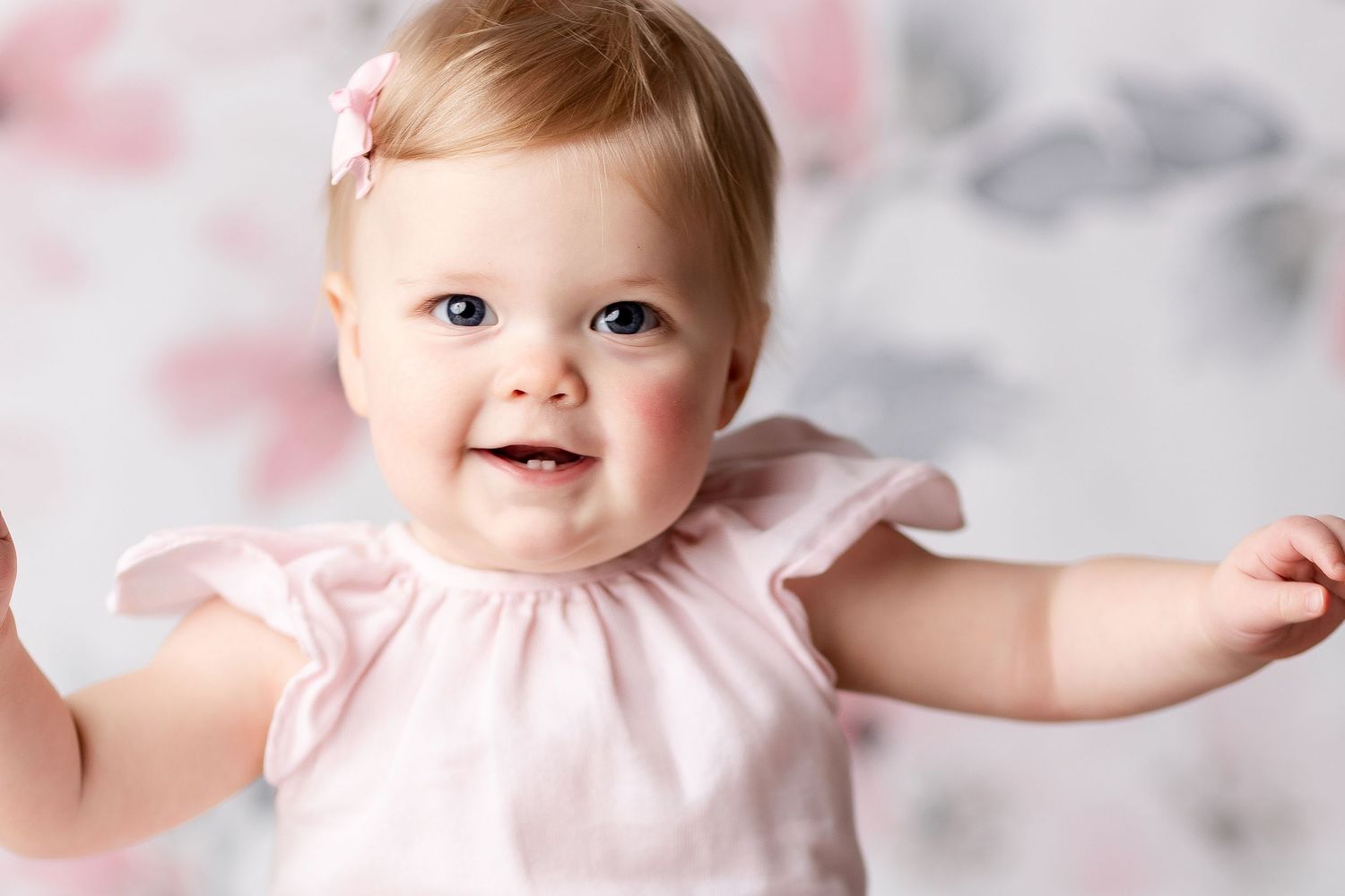Baby in pink dress smiles and reaches out during portrait session.
