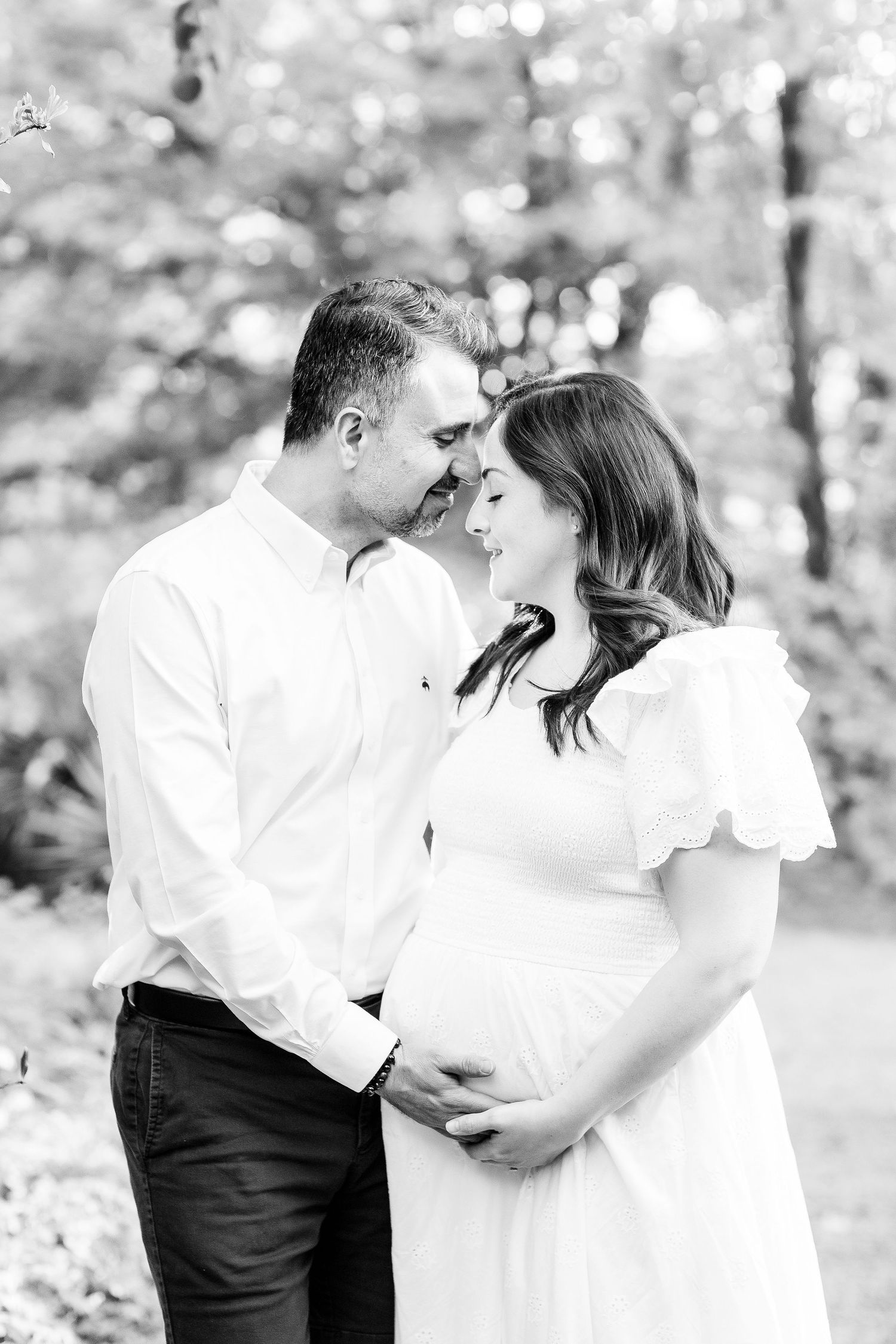 A romantic black and white photo series showing a couple in white clothing embracing outdoors in a natural setting.