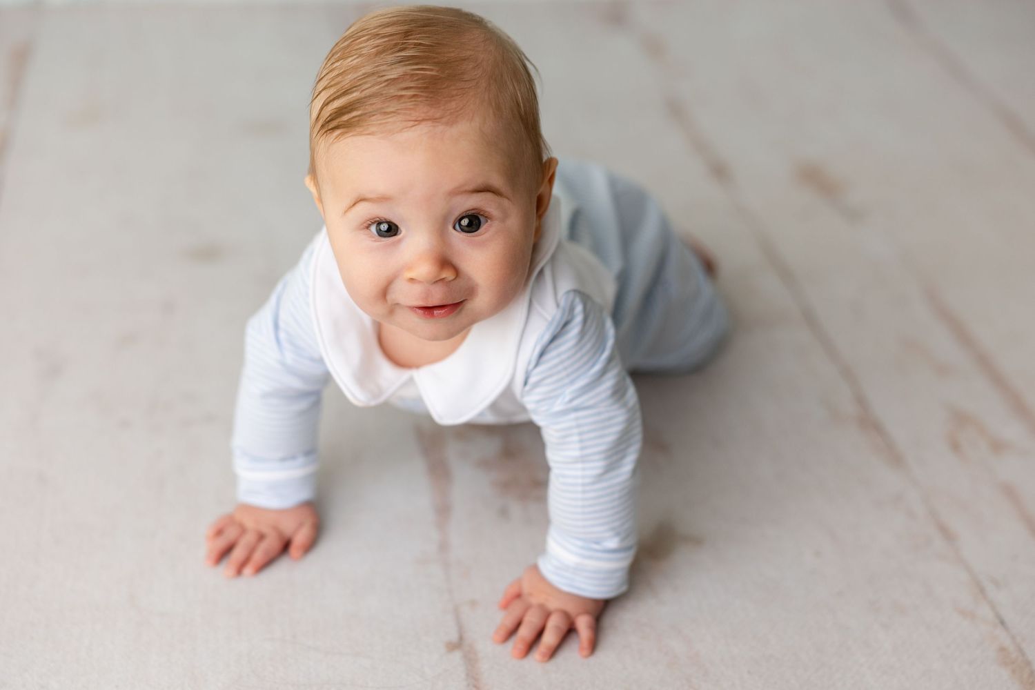 Baby wearing white onesie crawls on light marble floor in sequence of developmental milestone photos.