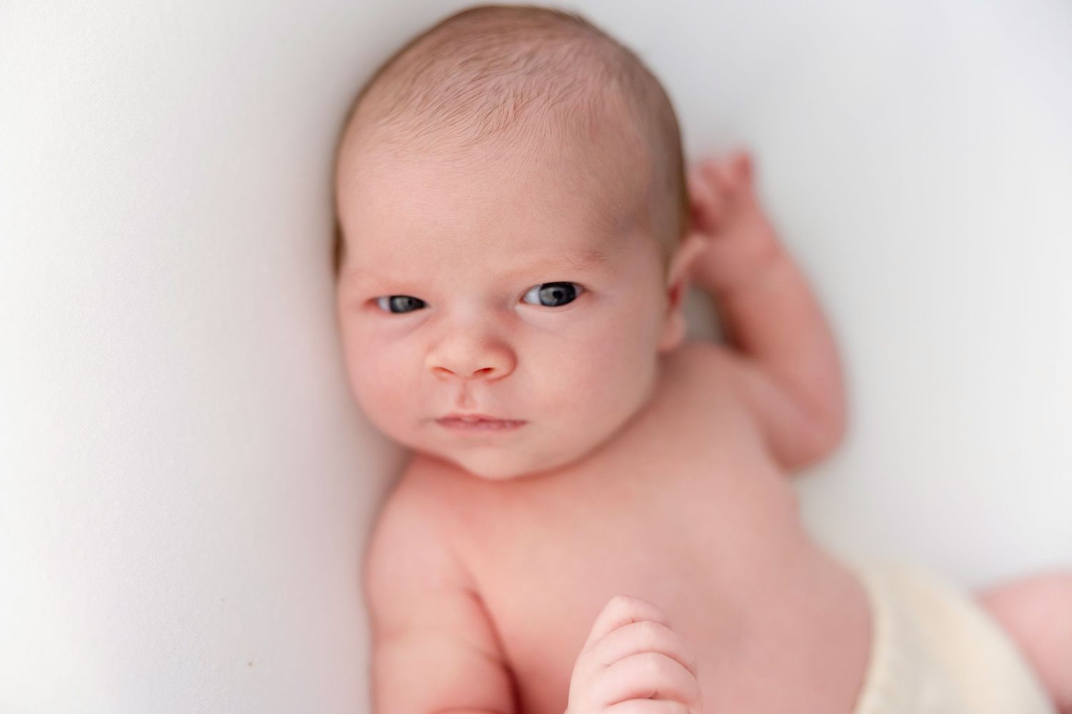 Newborn baby with blue eyes lying on a white background, looking alert and curious.