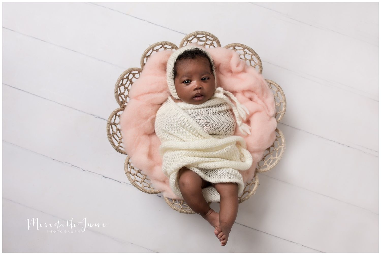A newborn baby lies peacefully on a pink blanket with lace trim in a professional photography setting.