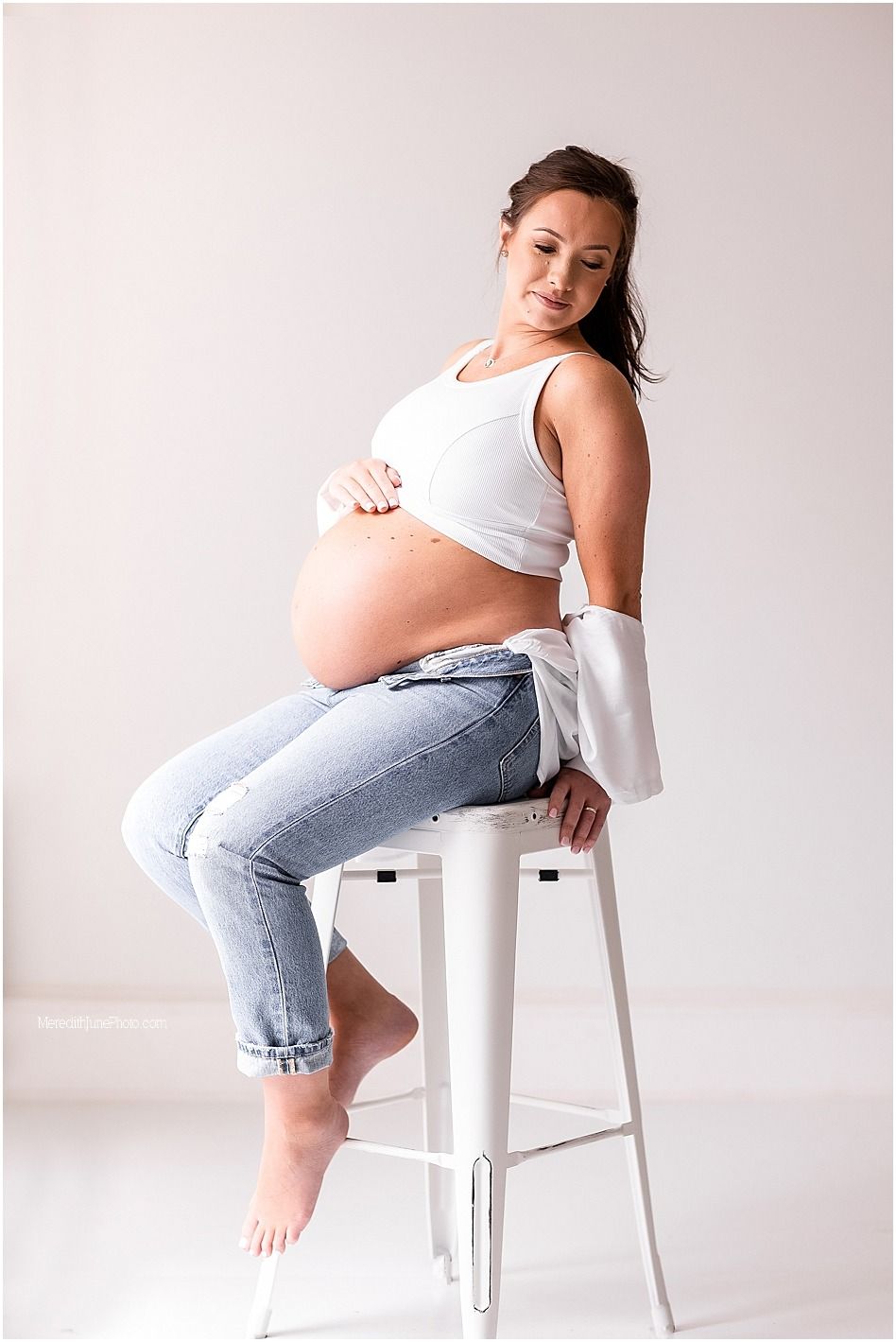 A series of minimalist maternity photos showing a pregnant woman in jeans and white top posing on a white stool.