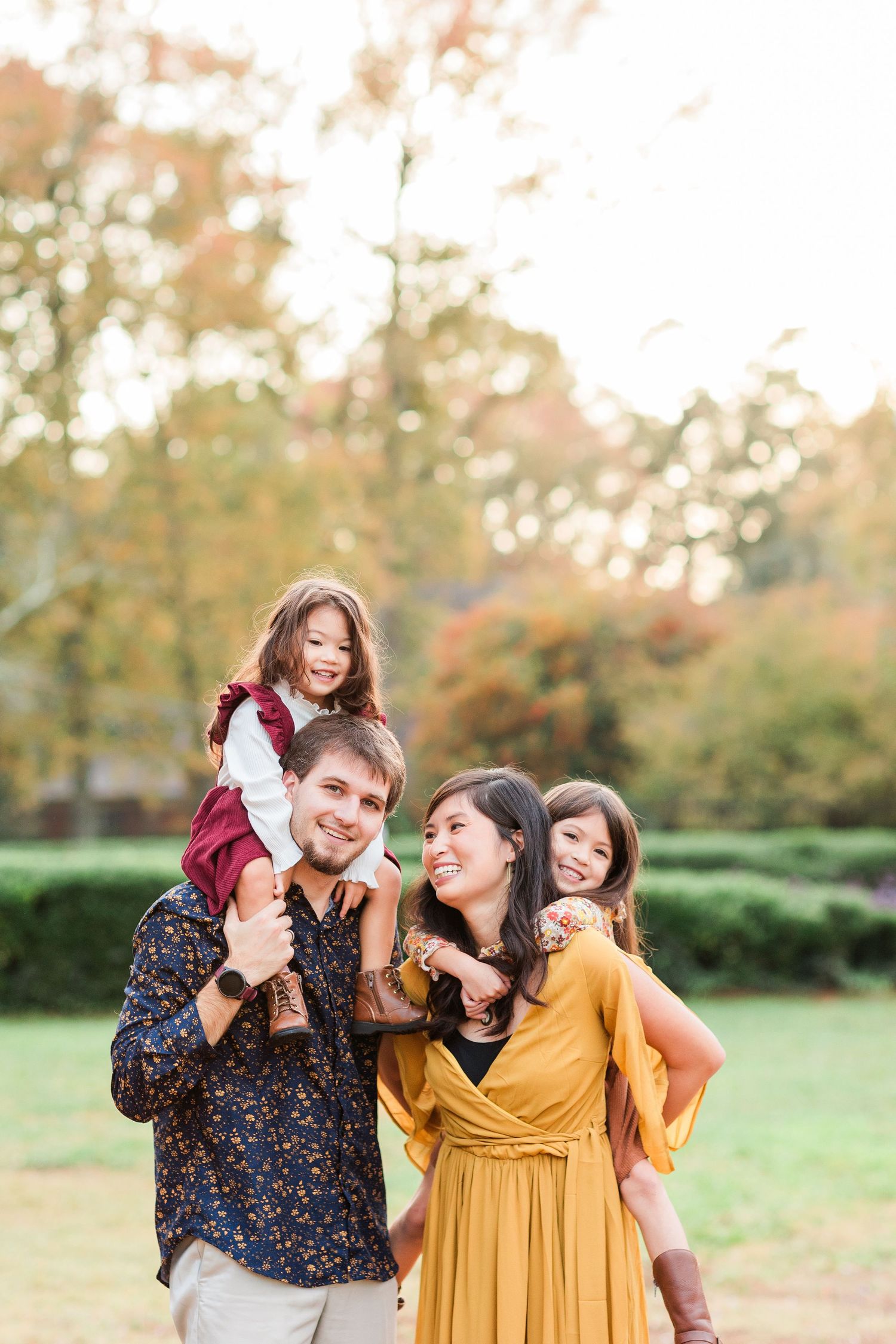 A joyful group shares laughter together in a park during golden hour with autumn foliage in the background.